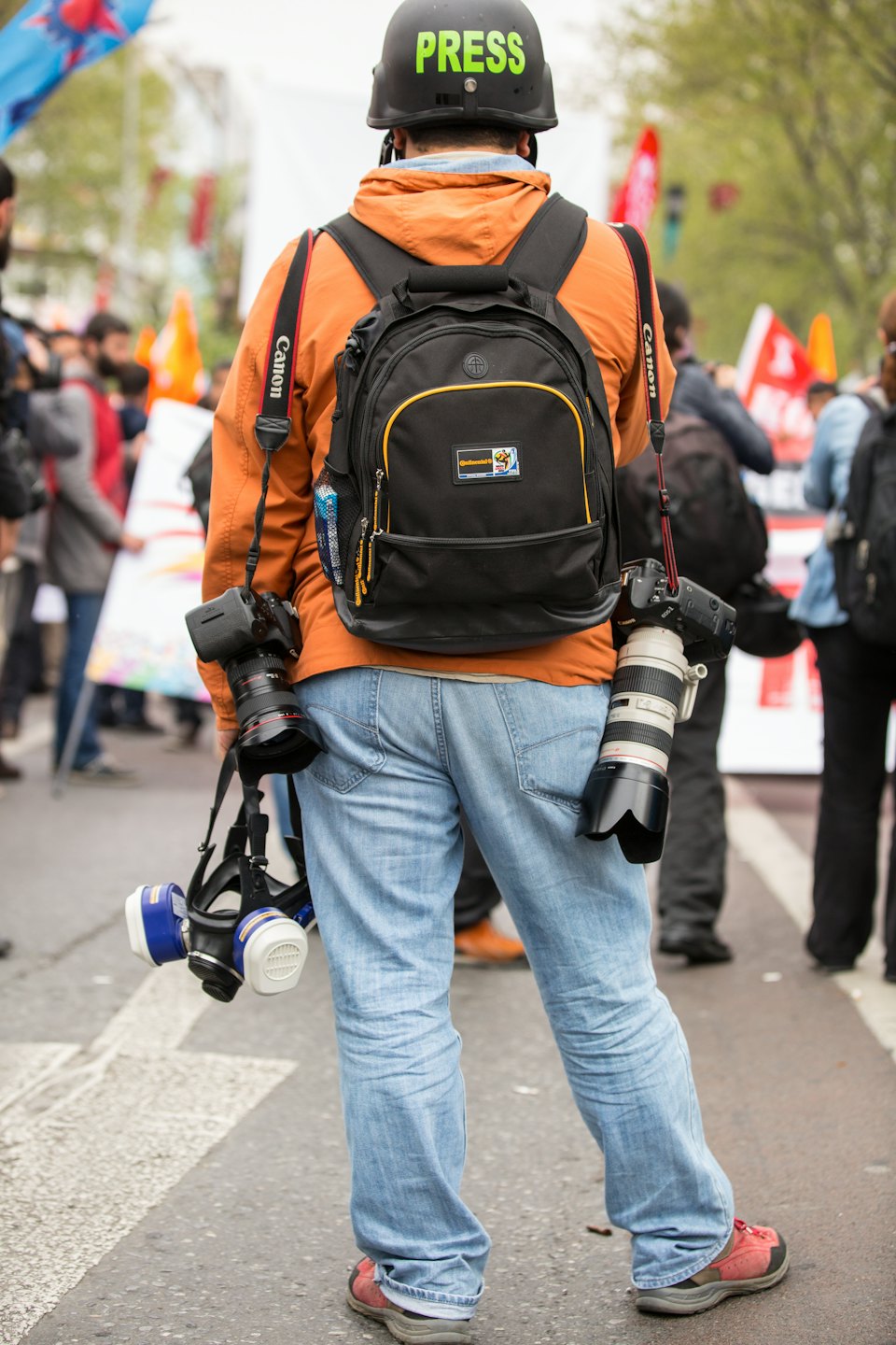 Fotojournalist in een oranje jas staat tussen een menigte.