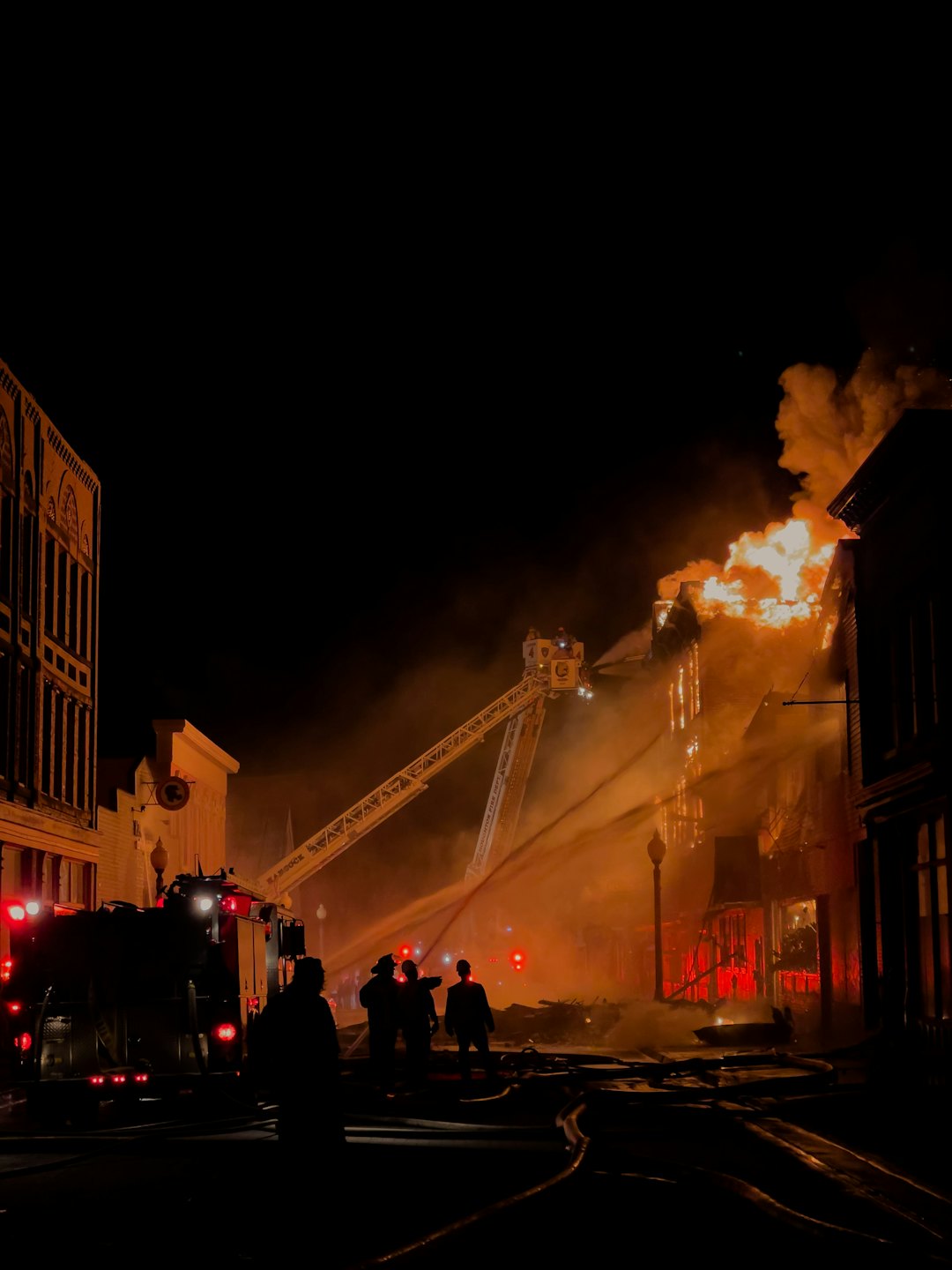 Brandweerlieden bestrijden 's nachts een grote brand in een gebouw met waterslangen.
