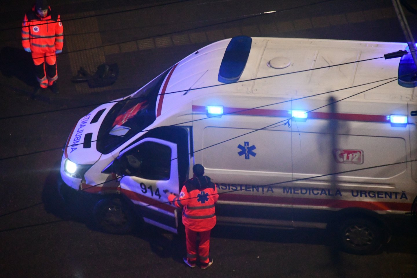Twee paramedici in oranje uniformen staan 's nachts bij hun ambulance.